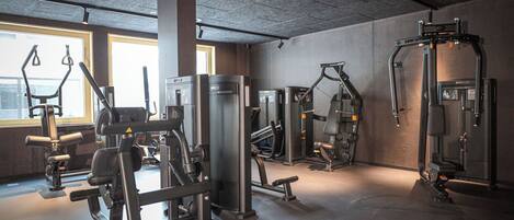A gym with various exercise machines, large windows, and a concrete ceiling.