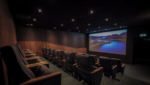 A dark theater with rows of black leather seats, a large screen, and a wooden panel wall. - Revier Mountain Lodge Saas-Fee (Saas-Fee)