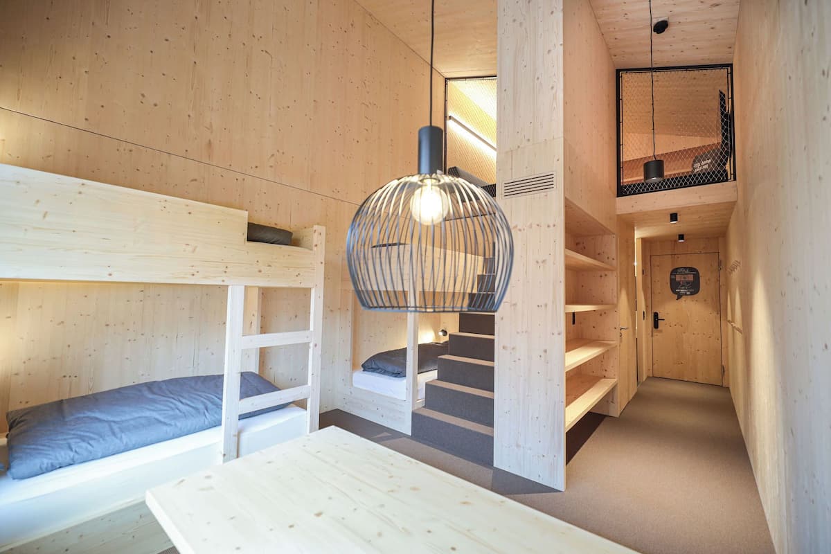Een compact, houten interieur met stapelbedden, een hanglamp en een trap naar een verdieping erboven.