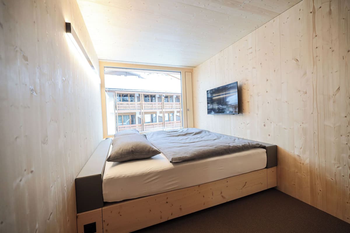 Een kamer met houten lambrisering, een bed, een raam en een lijst met een afbeelding aan de muur.