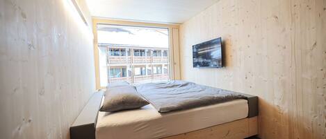 A wooden-paneled room with a bed, a window, and a framed picture on the wall.