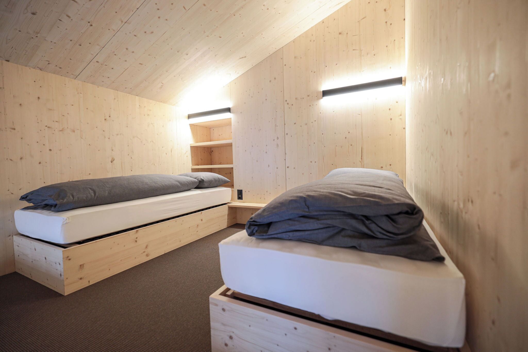 A small, cozy room with two wooden beds, built-in shelves, and a slanted ceiling.