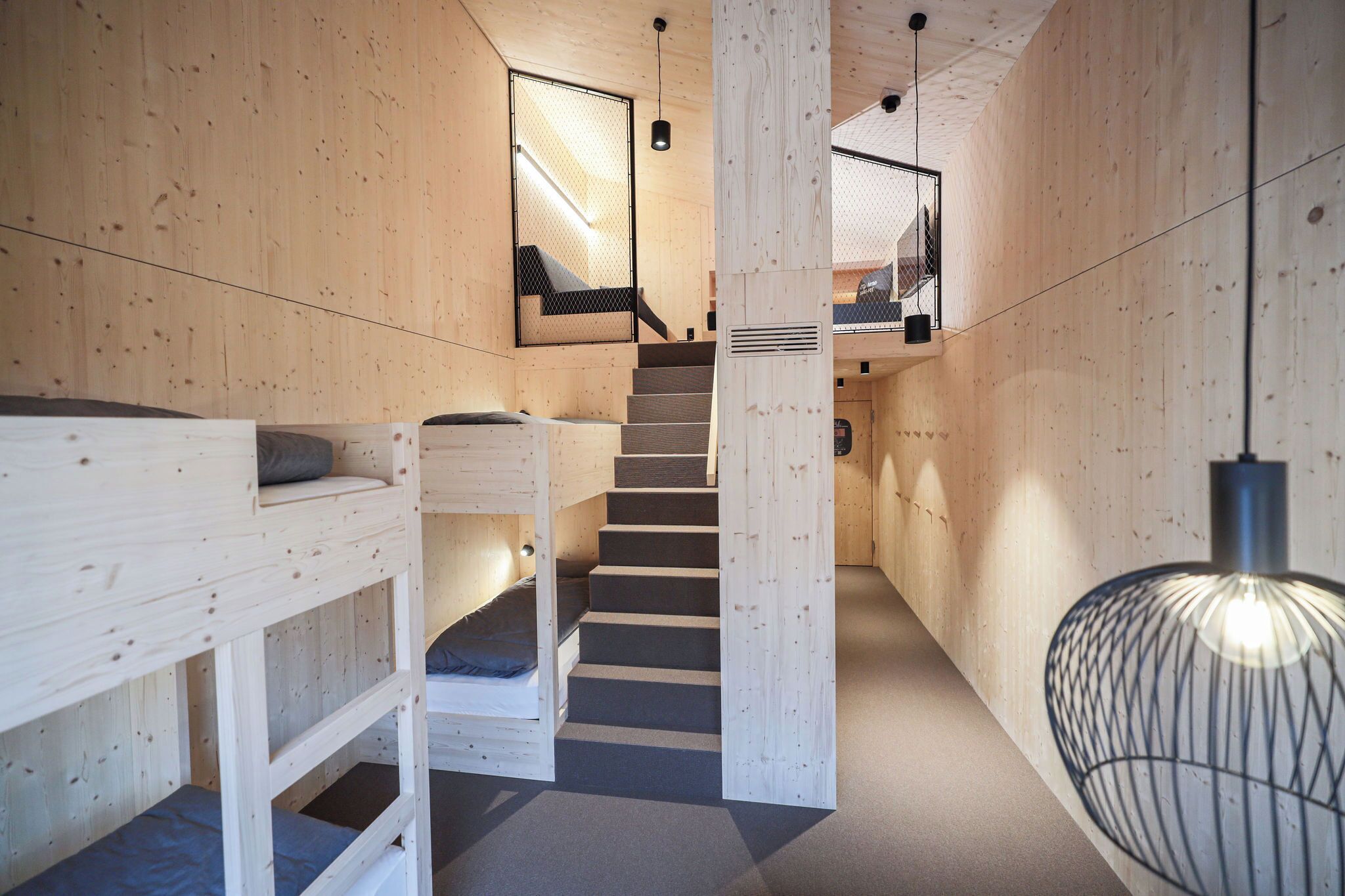 Interior de madera con literas, una escalera y una lámpara colgante.