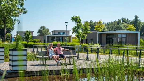 A couple sitting on a bench by a water feature with modern buildings in the background. - 55 by the Water (Olburgen)