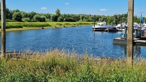 A calm river with boats docked at a marina, surrounded by greenery and a clear sky. - 55 by the Water (Olburgen)