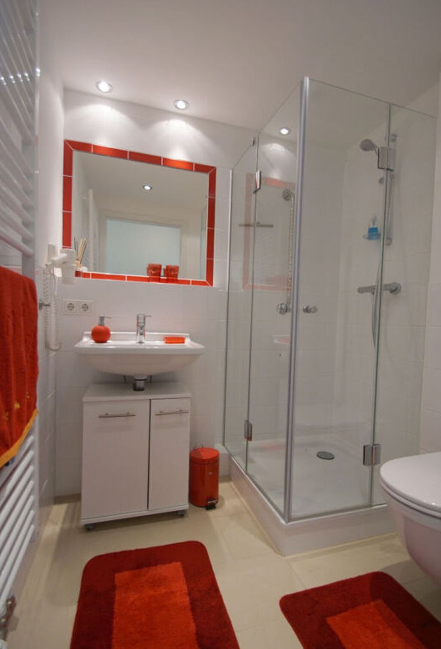 A modern bathroom with a glass shower enclosure, a white sink, and a red accent wall.