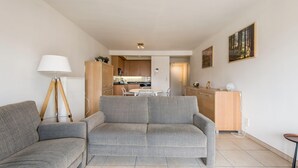 Un soggiorno con un divano grigio, una lampada e una cucina sullo sfondo.