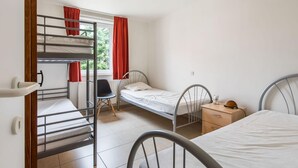 Una camera del dormitorio con letti a castello, un letto singolo, una sedia, un comodino e una finestra con tende.