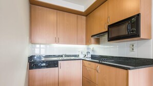 Una cucina compatta con mobili in legno, un forno a microonde nero, un forno integrato, un lavello e una macchina da caffè.