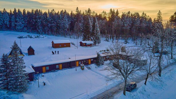 A cabin complex surrounded by snow-covered trees, with a clear sky and a sunset in the background. - "sporthütten Nassau" Ihr Zentrales Domizil an der Blockline (Frauenstein)