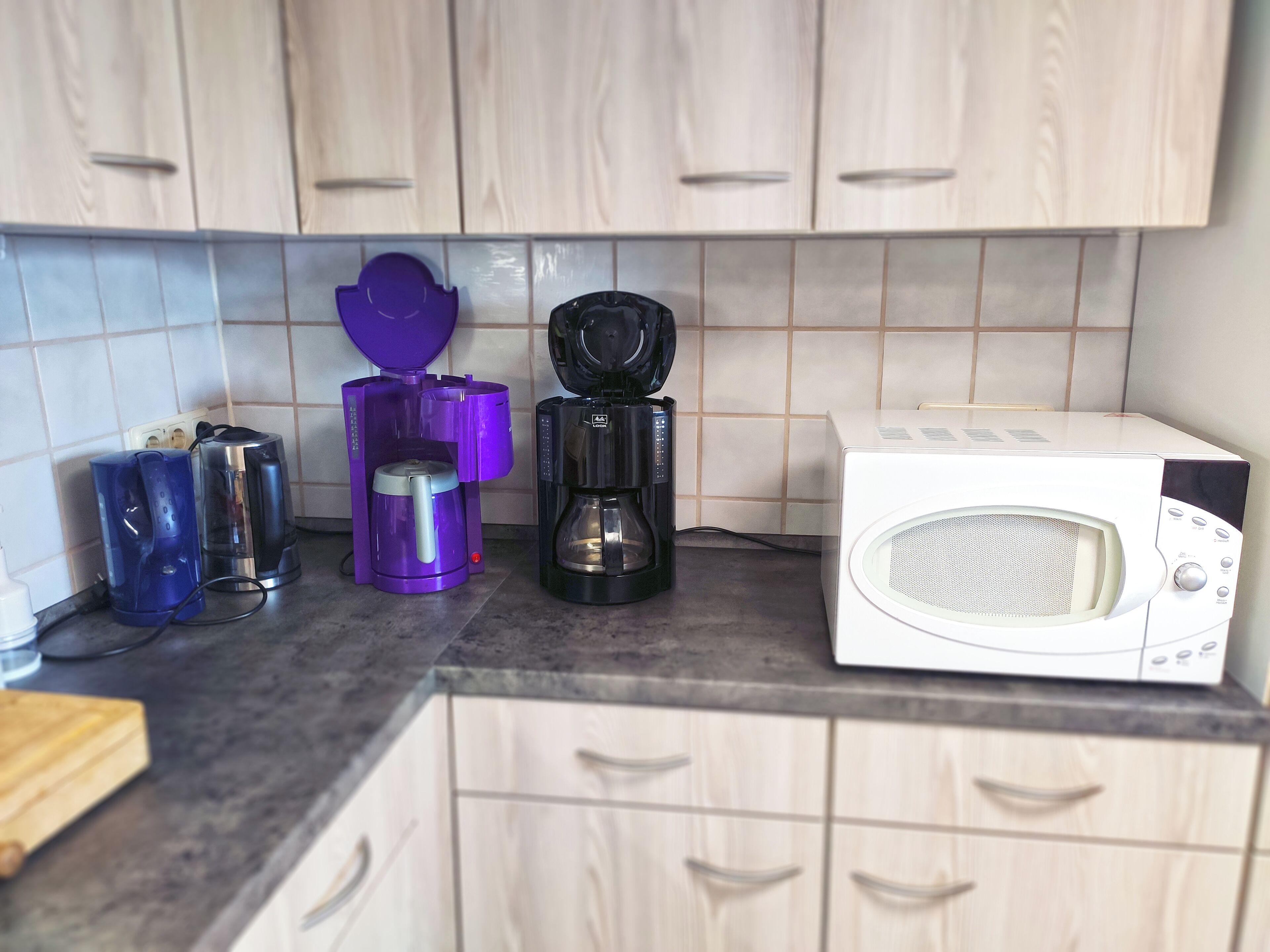 Una cucina con pensili e basi in legno, un forno a microonde, una macchina per il caffè e un tostapane.