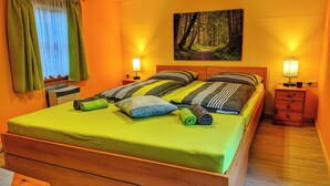 A bed with green bedding, striped pillows, and rolled towels. There are two bedside tables with lamps, a painting of a forest on the wall, and a window with curtains. - "sporthütten Nassau" Ihr Zentrales Domizil an der Blockline (Frauenstein)