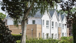 A row of modern, two-story houses with a mix of white and wooden facades, surrounded by well-maintained gardens and trees. - Fischer Heiligenhafen 4d (Heiligenhafen)