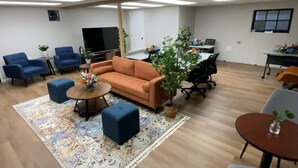 A spacious room with a sofa, two armchairs, a coffee table, and a small table with a plant. There is a TV and a desk with a computer. - Conference Room Rental no sleeping arrangements  (Cromwell)