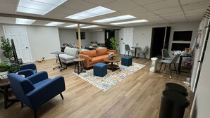 A spacious room with a wooden floor, a sofa, blue armchairs, a coffee table, and a rug. - Conference Room Rental no sleeping arrangements  (Cromwell)