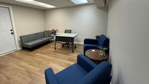 A room with a grey sofa, a blue armchair, a small table with a vase, and a white door. - Conference Room Rental no sleeping arrangements  (Cromwell)