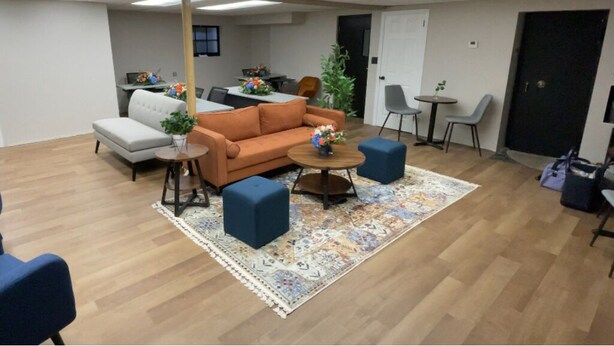 A modern office space with a sofa, two round tables, and a coffee table. There are chairs around the tables, a rug on the floor, and a door in the background. - Conference Room Rental no sleeping arrangements  (Cromwell)