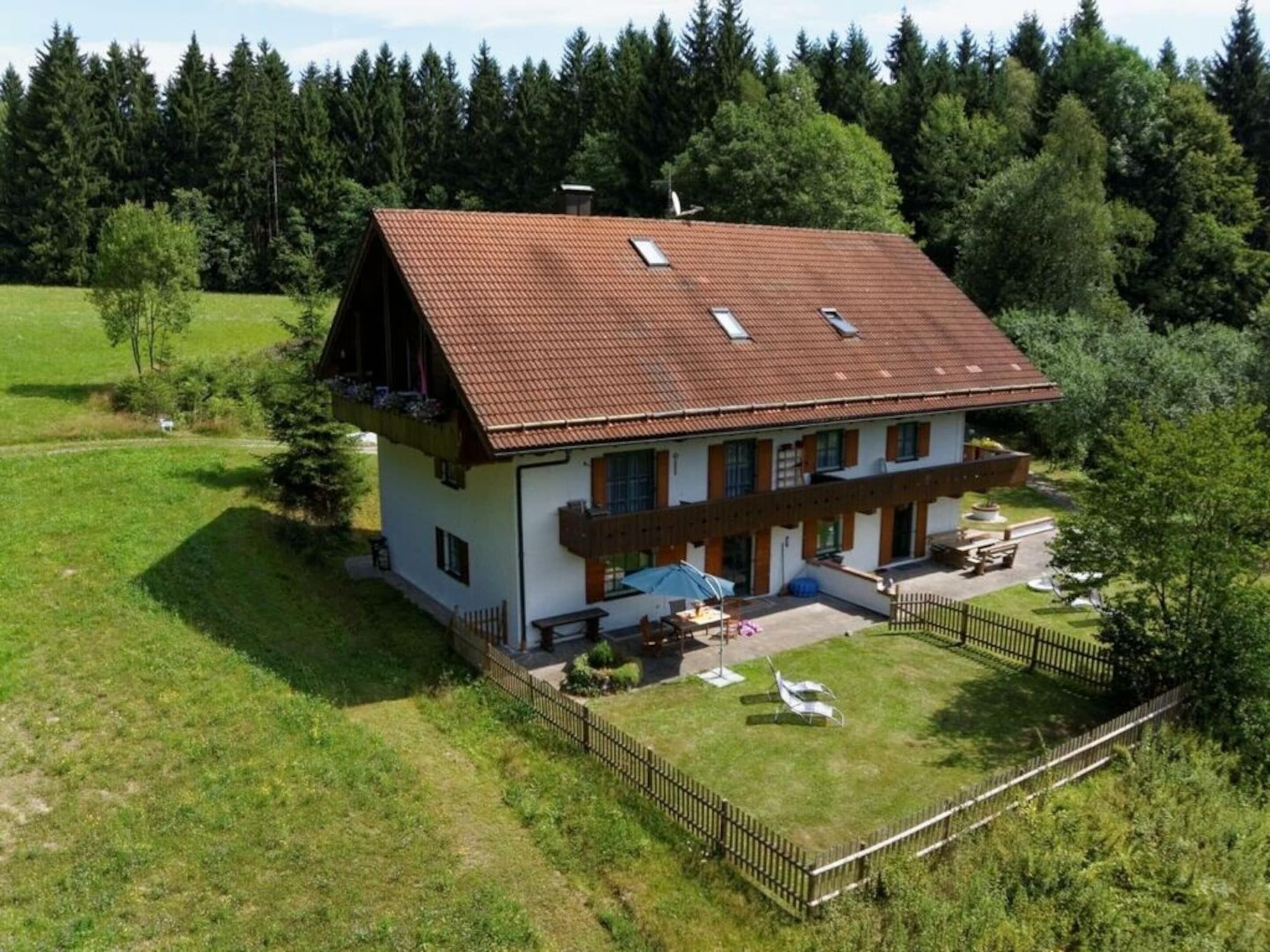 Ein zweistöckiges Haus mit geneigtem Dach, einem Balkon und einem umzäunten Garten.