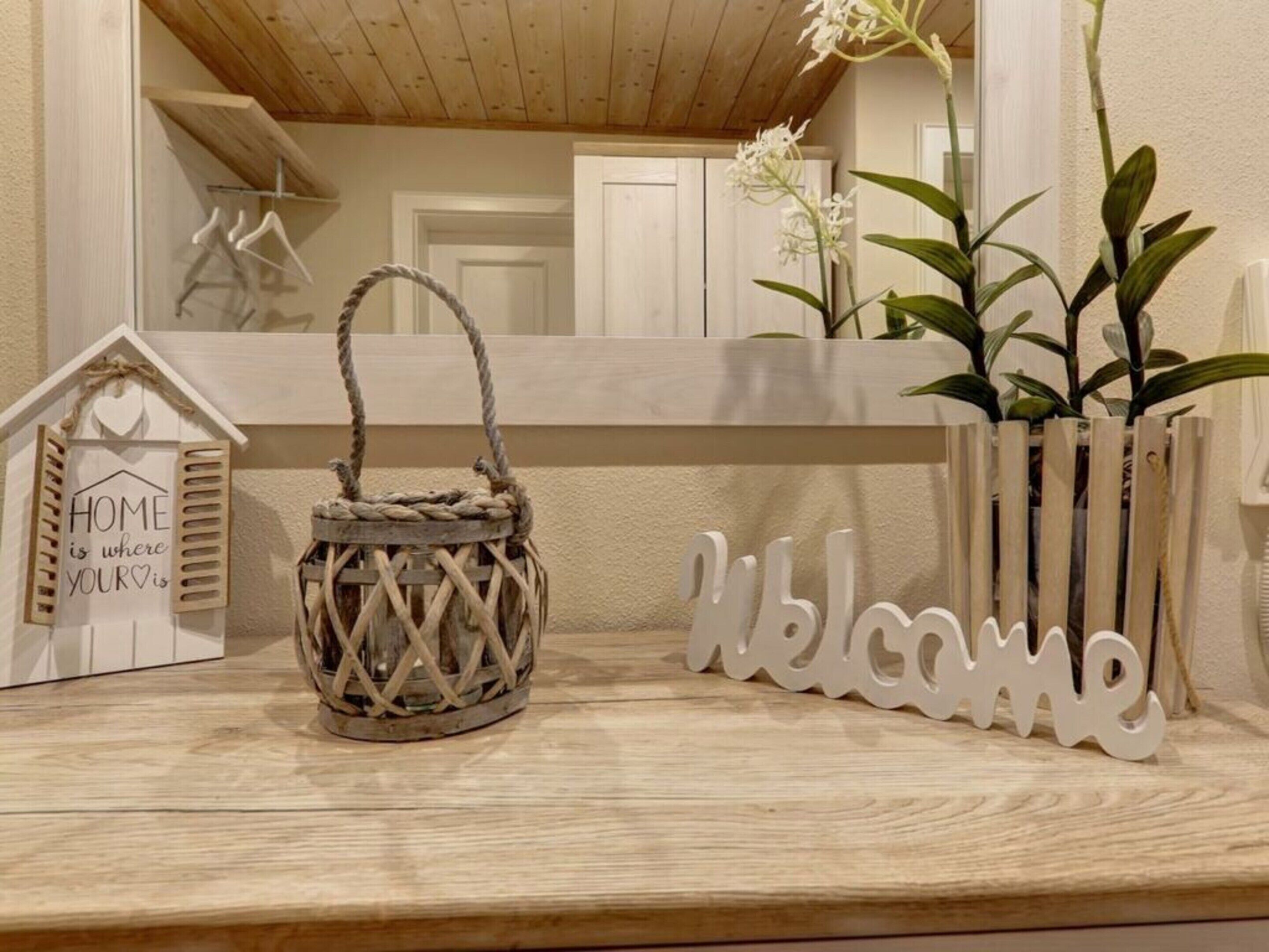 A wooden shelf with a welcome sign, a wicker basket, and a small house-shaped sign with a heart.
