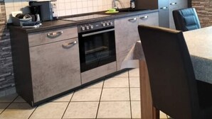 Eine moderne Küche mit Einbauofen, Mikrowelle und Kaffeemaschine. Ein Esstisch mit Stühlen und eine Anrichte mit Fernseher sind ebenfalls vorhanden.