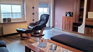 Ein Wohnzimmer mit einem schwarzen Ledersessel, einem Holztisch, einer Couch und einer Anrichte mit Lautsprechern.