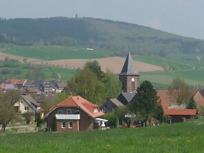 A rural village with traditional houses, a church, and rolling hills in the background.