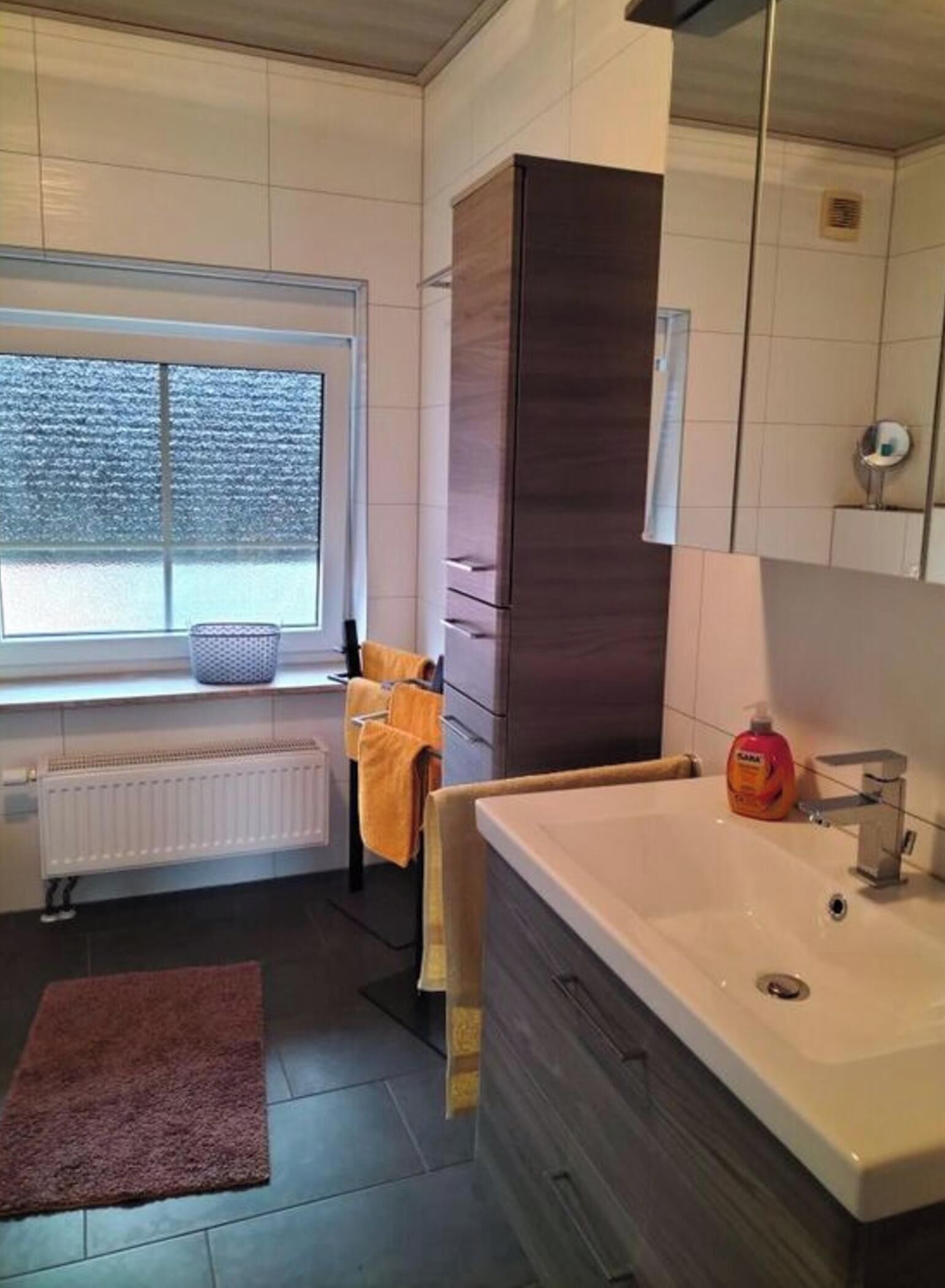 Un baño moderno con un ventanal amplio, un lavabo blanco y un espejo.
