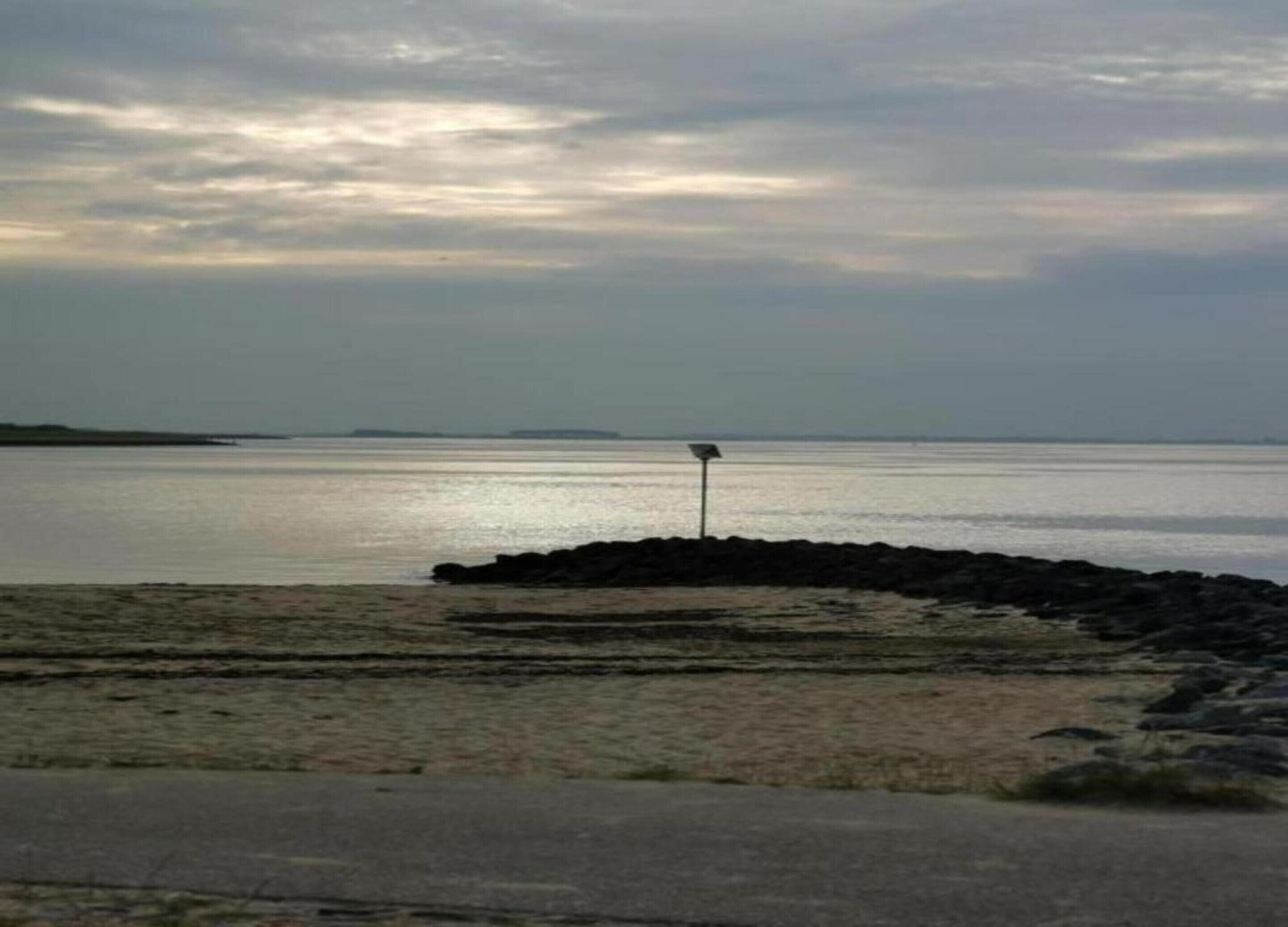 A beach with a rocky shoreline and a signpost in the distance.