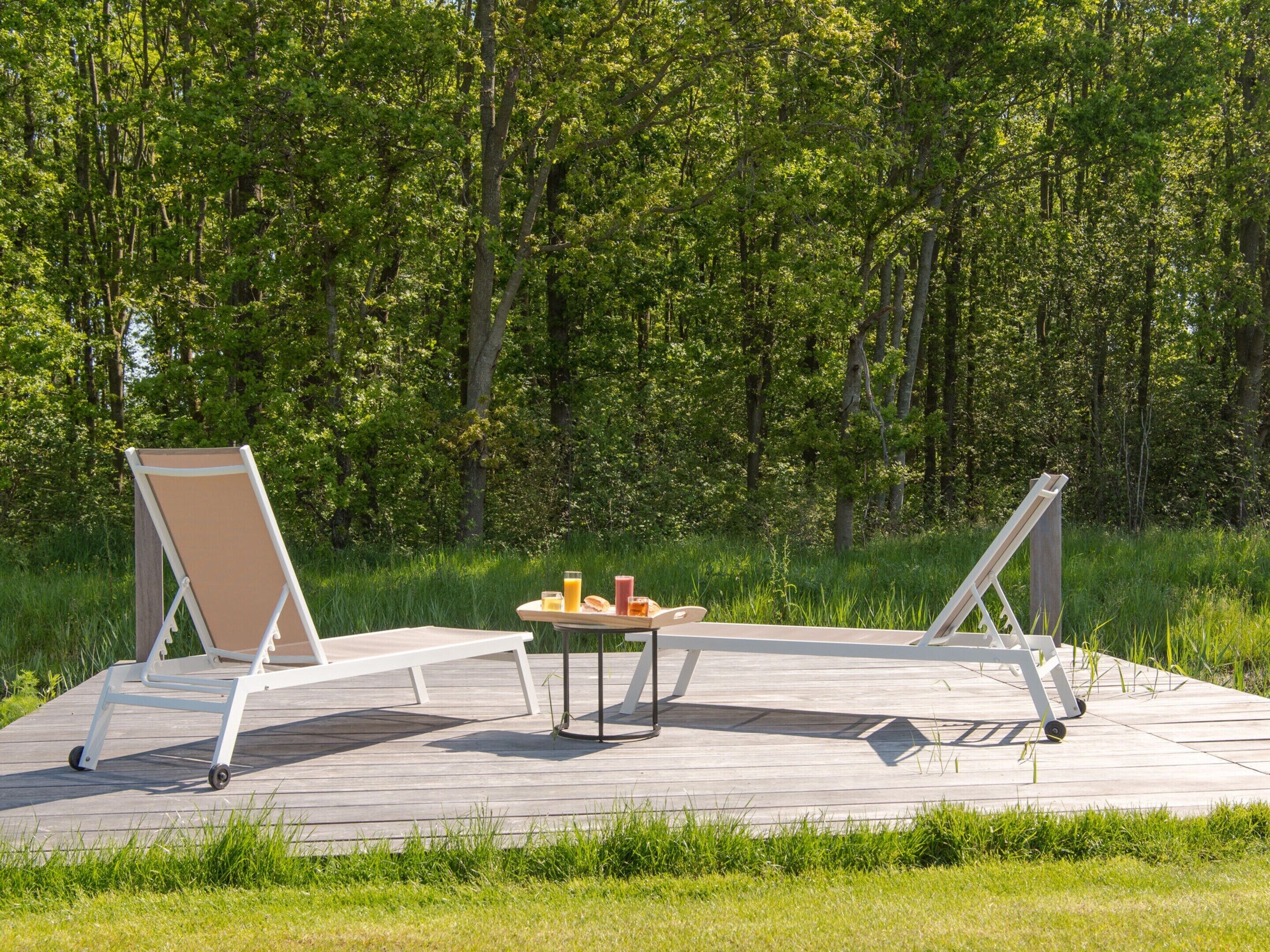 A wooden deck with two lounge chairs and a table with drinks.