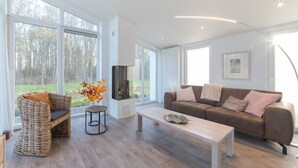 A spacious living room with large windows, a fireplace, a sofa, and a coffee table. - Cozy Zeeland Getaway Spot (Wemeldinge)