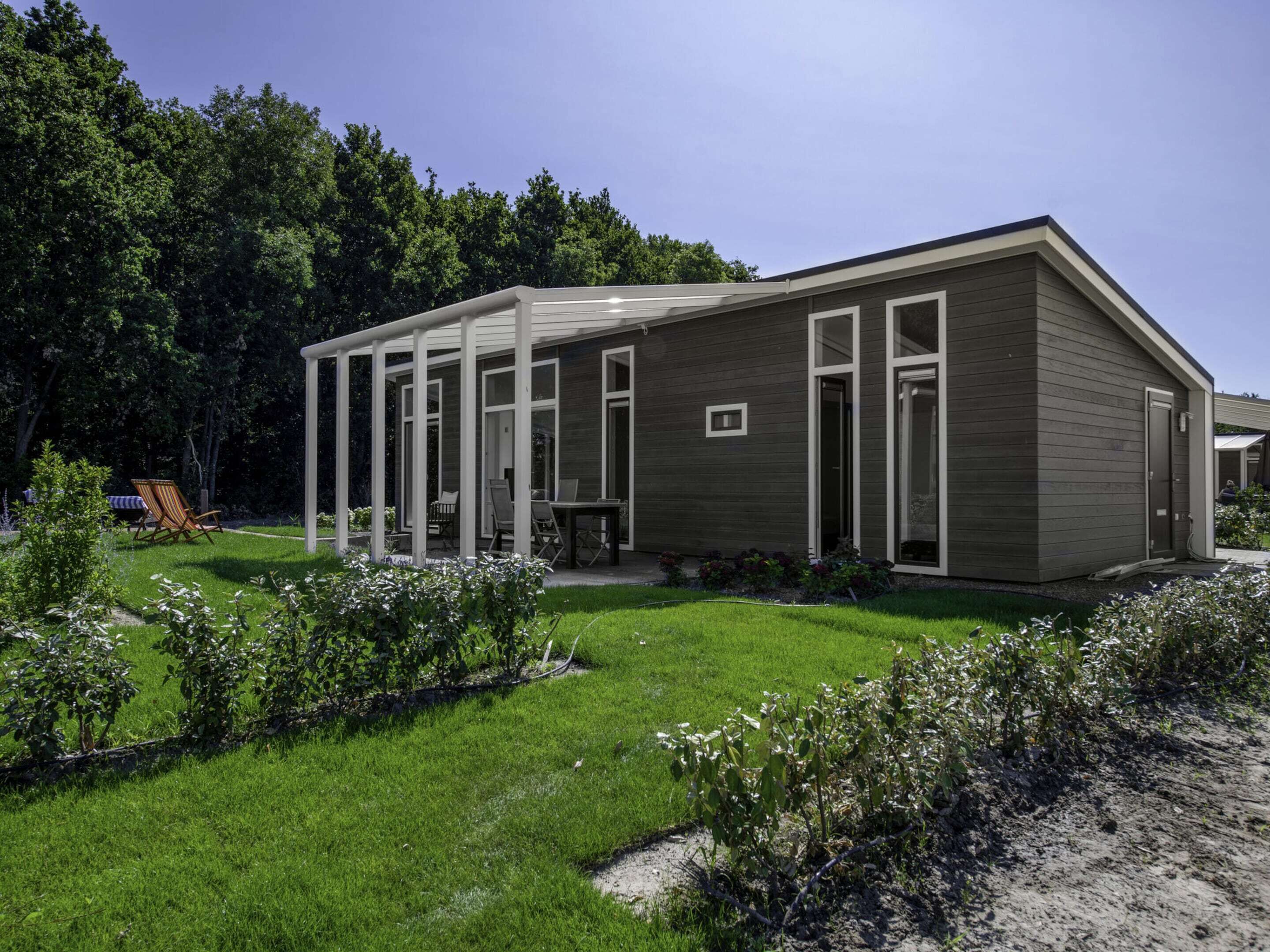 Een modern huis met een overdekt terras, een gazon en een tuin.