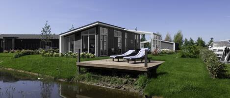 A modern building with a deck and lounge chairs by a pond.