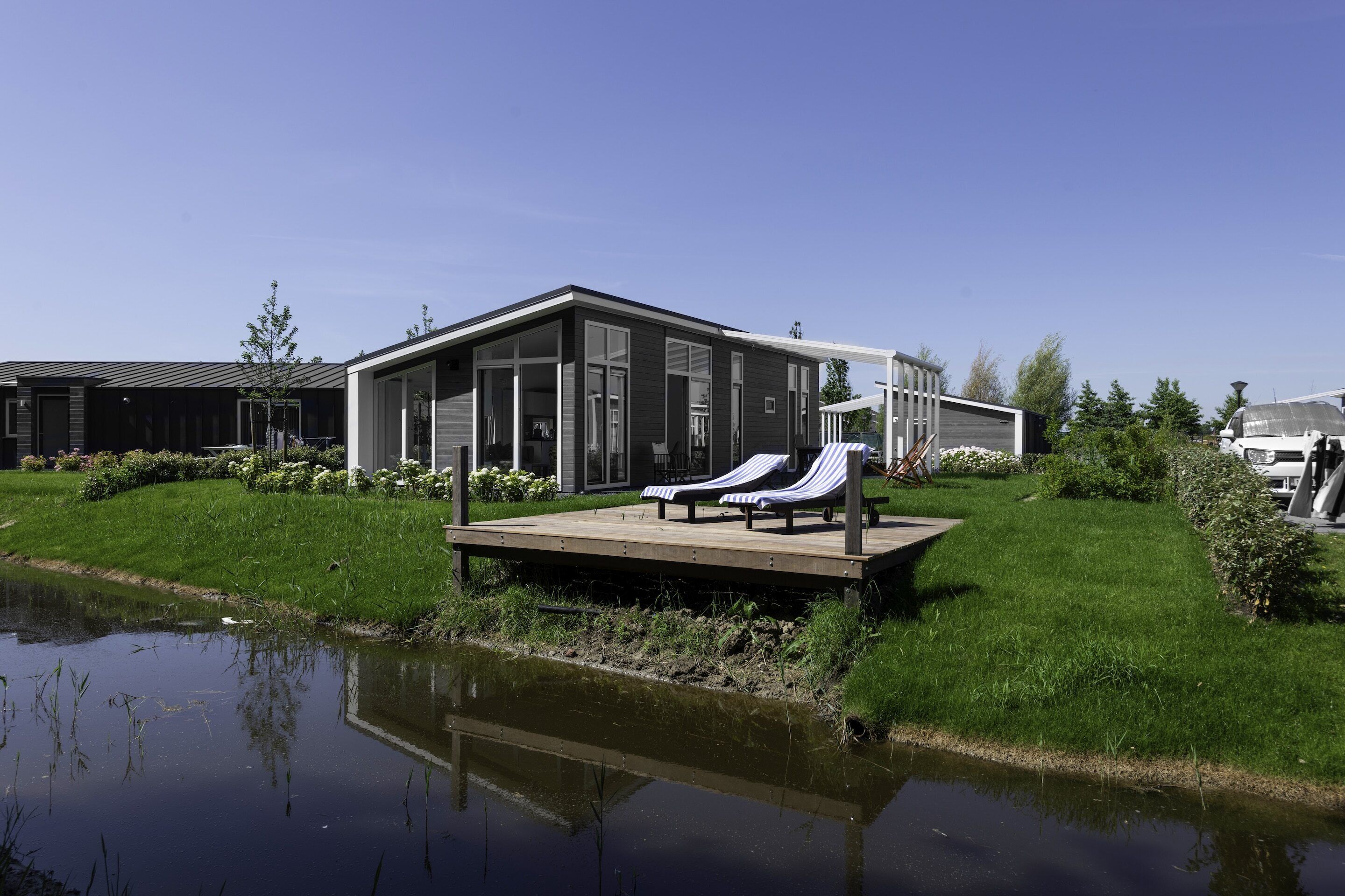A modern building with a deck, two lounge chairs, and a pond.