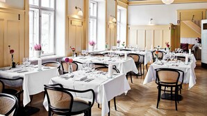 A restaurant with multiple tables set for dining, featuring white tablecloths, wicker chairs, and floral centerpieces.