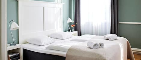 A neatly made bed with white linens, a bedside lamp, and a bedside table with a book and a vase of flowers.