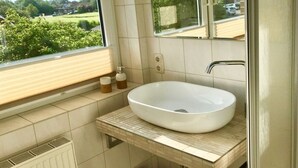 A bathroom with a large window, a white sink, and a mirror. - Family and dog Hafenblick (Wittmund)