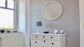 A white dresser with a round mirror above it, a lamp, and two small picture frames. - Family and dog Hafenblick (Wittmund)
