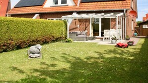 A house with a sloped roof, solar panels, a covered patio, and a well-maintained garden. - Family and dog Hafenblick (Wittmund)