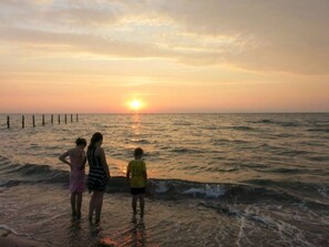 A sunset over the ocean with three people standing in shallow water. - Farm Ferienhof Albert (Gremersdorf)