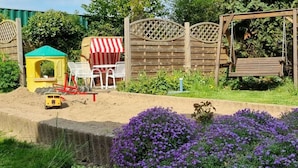 Un jardín con zona de juegos, valla de madera y diversas plantas.