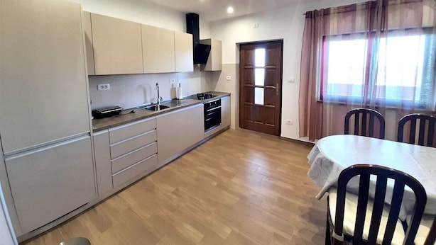 A compact kitchen with a sink, stove, and cabinets, a dining area with a table and chairs, and a door leading to another room. - Apartment Tre Pini 2 with sea view (Umag)