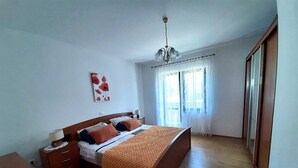 A bedroom with a wooden bed, a nightstand, a desk, a chair, a rug, and a window with curtains. - Apartment Tre Pini 2 with sea view (Umag)