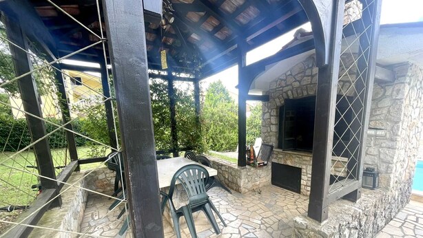 An outdoor patio with stone flooring, a stone fireplace, and a covered seating area with a table and chairs. - Apartment G&G Red with swimming pool (Poreč)