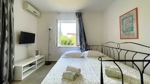 A bedroom with a bed, a TV, a window, and a painting on the wall.