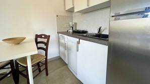 A compact kitchen with white cabinets, a dishwasher, a refrigerator, and a small dining table with a chair.