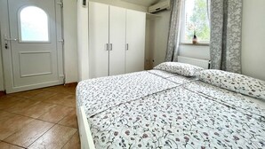 Makuuhuone, jossa on sänky, vaatekaappi, ikkuna verhoilla ja patteri.