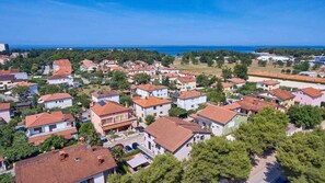 Une vue aérienne d’un quartier résidentiel avec des maisons, dont certaines ont des toits recouverts de tuiles rouges, et une vue dégagée sur la mer en arrière-plan.