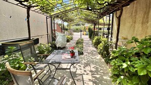 Een overdekt terras met een tafel en stoelen, omringd door potplanten en een pergola.