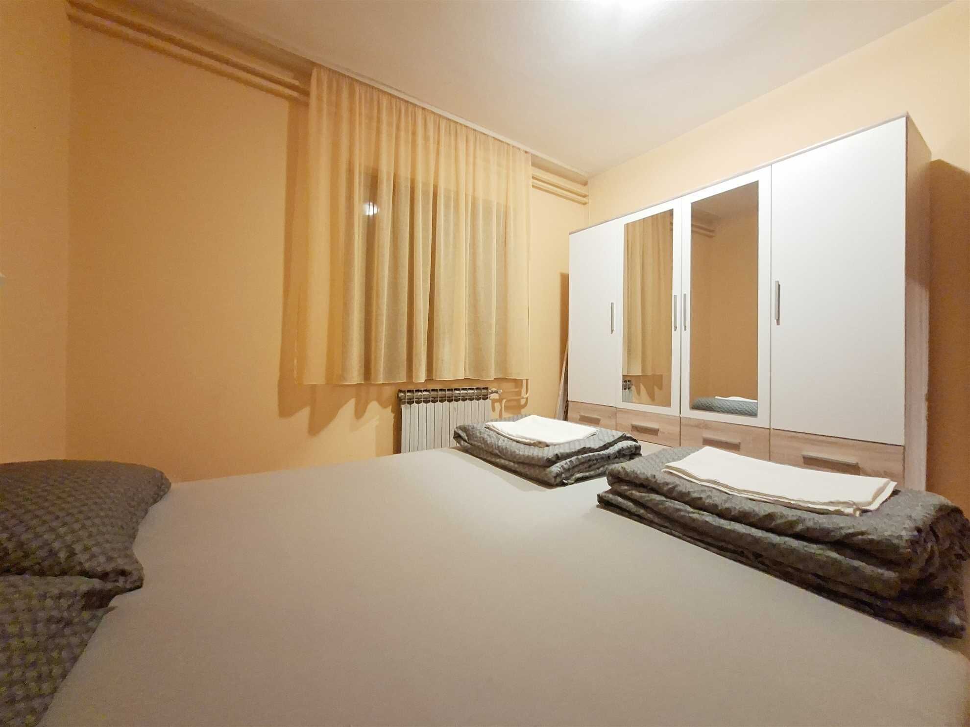 A hotel room with a bed, a wardrobe, a radiator, and a window with curtains.