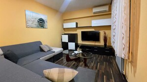 Een moderne woonkamer met een bank, een glazen salontafel, een flatscreen televisie en een schilderij aan de muur.